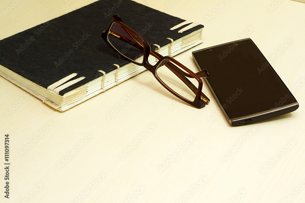 Glasses, black notebook and smartphone on wooden background. Glasses, black notebook and smartphone on wooden background.