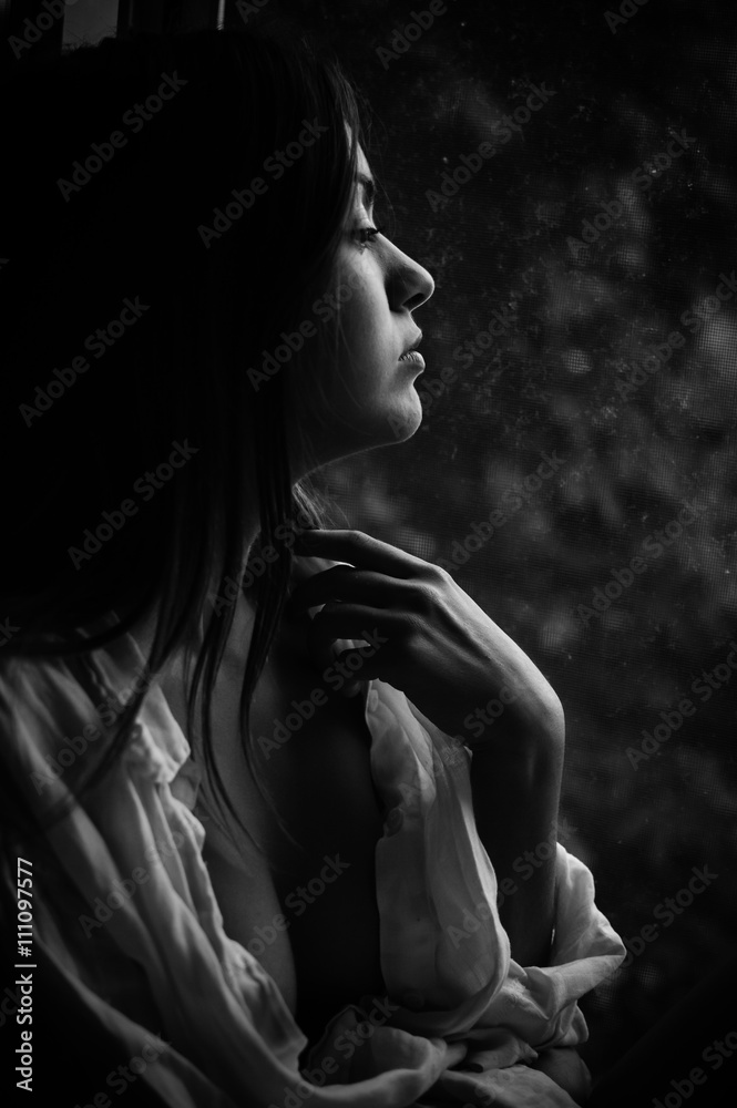 Black and white photography closeup of young pretty woman at the window looking outside Black and white photography closeup of young pretty woman at the window looking outside