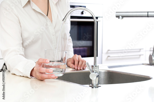 Pouring fresh water from ozone filter into the glass by woman in kitchen