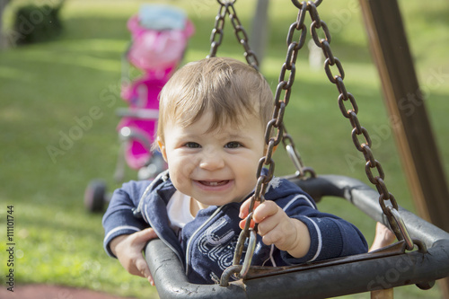 happy baby girl looking at camera while sitting on swing