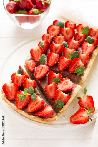 Homemade tart with strawberries and strawberry curd decorated mint leaves on white wooden background