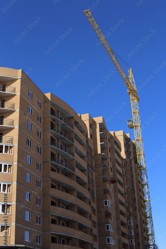 Fototapeta premium beautiful building and a successful businessconstruct highest building of orange brick. standing next to a construction crane. blue sky