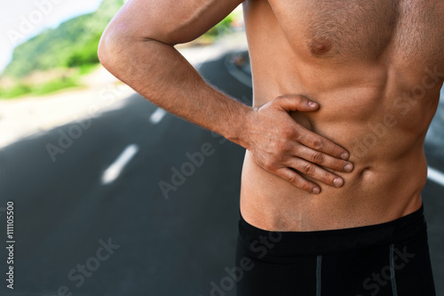 Stomach Ache. Closeup Of Athletic Fit Muscular Male Body With Hand Touching Belly. Handsome Fitness Man Suffering From Abdominal Pain And Feeling Bad After Running Outdoors. Sport Injury Concept