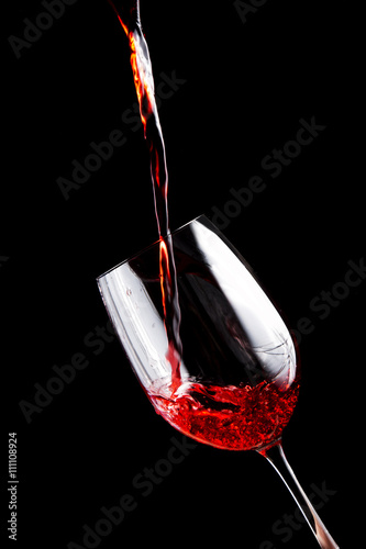 Red wine pouring into a wine glass. Isolated on black background. 