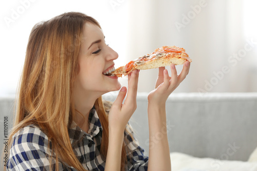 Happy young woman eating slice of hot pizza at home