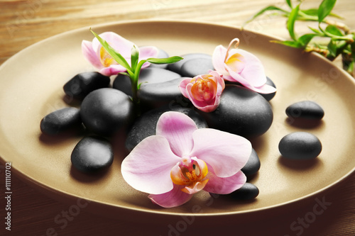 Spa stones and orchid flowers in plate on wooden table closeup
