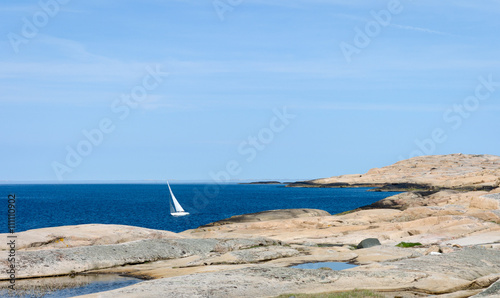 Small sailboat leans over close to the smooth rocks. Bright sunshine. photo