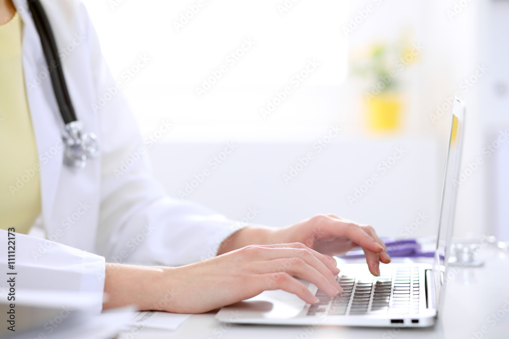 Close-up of female doctor typing laptop sitting at a table in the hospital Close-up of female doctor typing laptop sitting at a table in the hospital