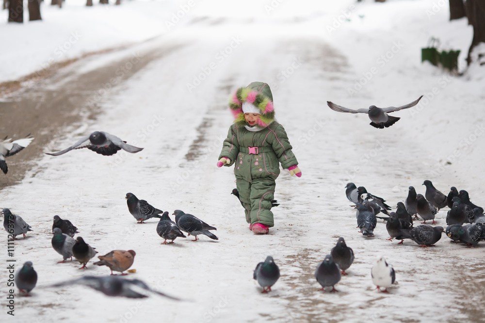 Child runs through a flock of pigeons on the square in winter city park Child runs through a flock of pigeons on the square in winter city park