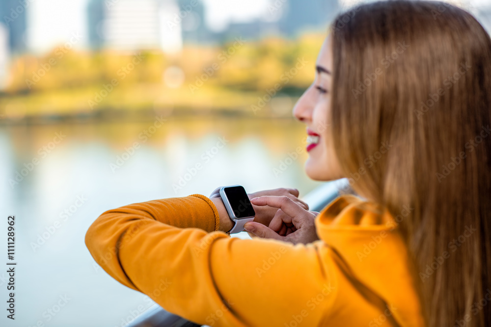 Young woman in yellow sweater using smart watch on the modern bridge with skyscrapers on the background. Sport application on the smart watch Young woman in yellow sweater using smart watch on the modern bridge with skyscrapers on the background. Sport application on the smart watch