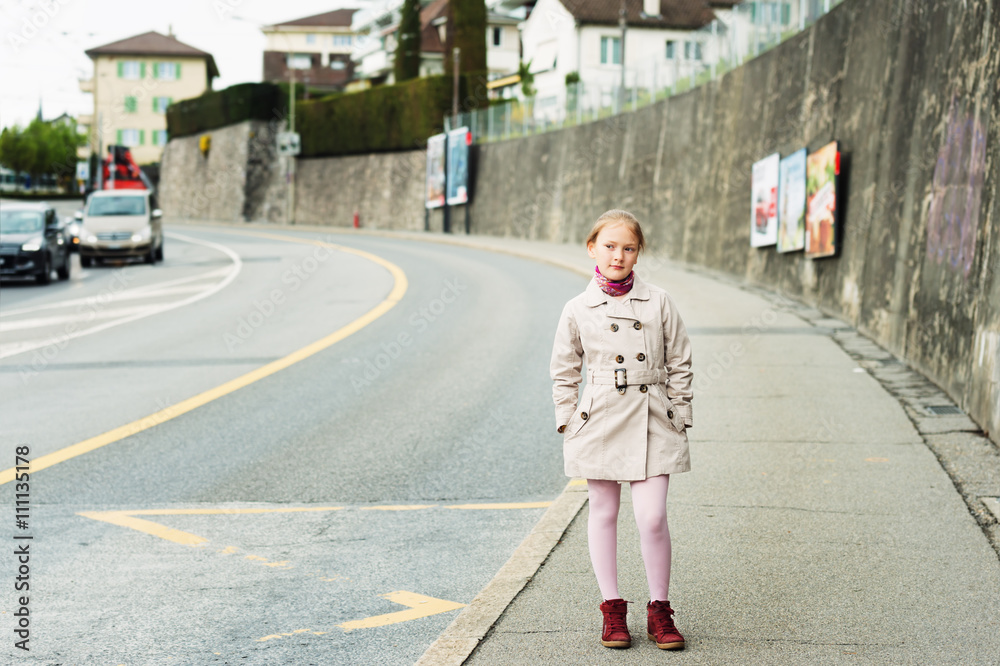 Outdoor portrait of a cute little girl, wearing beige coat and red shoes