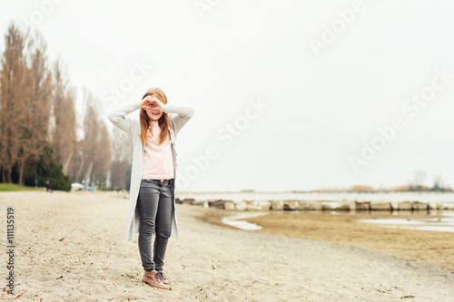 Adorable little girl of 8-9 years old playing by the lake, wearing grey trousers and long cardigan © annanahabed