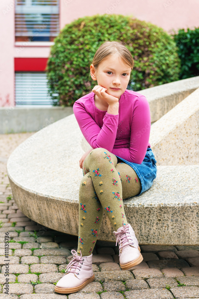 Fashion portrait of a cute little girl in a city, wearing pink shoes,  t-shirt, denim skirt and green tights Stock Photo
