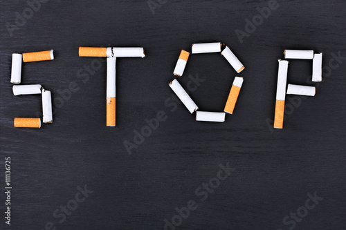 the inscription "stop" is lined with a large number of cigarettes with orange filter on black wooden background