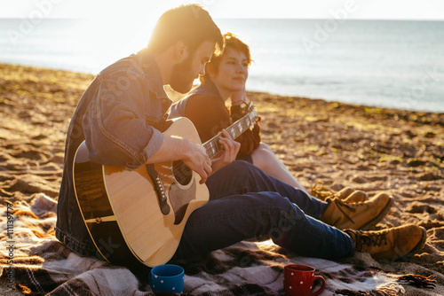 young caucasian couple playing guitar on beach at sunset
