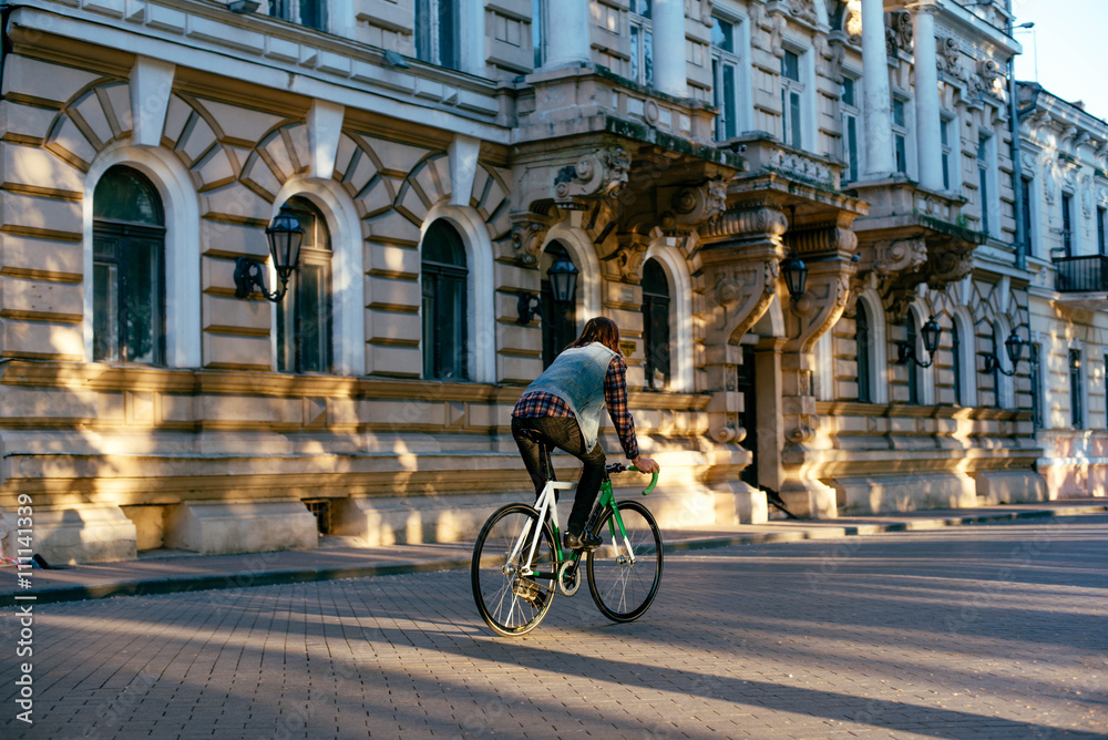 young brunette man riding fixed-gear bicycle in the city on a sunny day