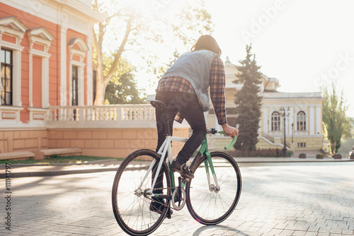 young brunette man riding fixed-gear bicycle in the city on a sunny day