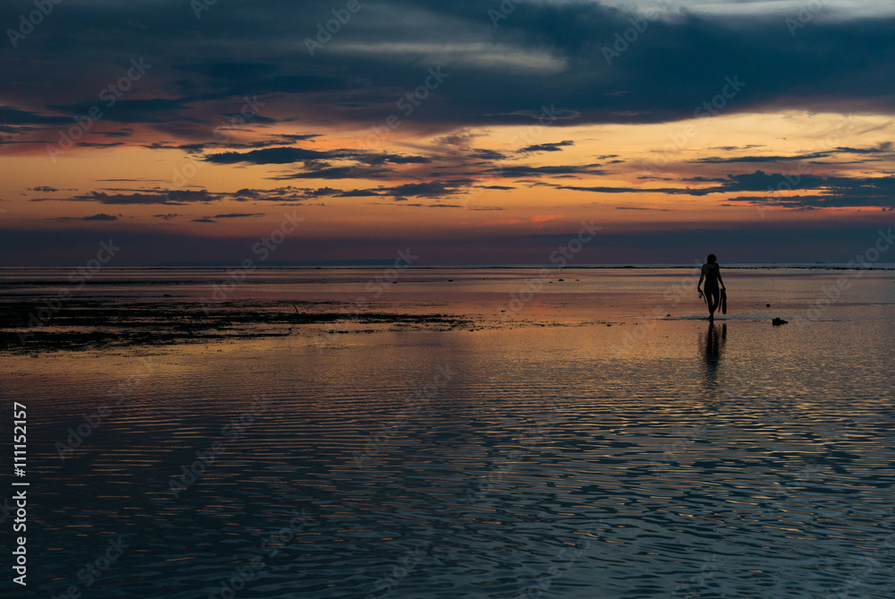 Sunset and silhouette of woman with snorkeling gears on Gili Air