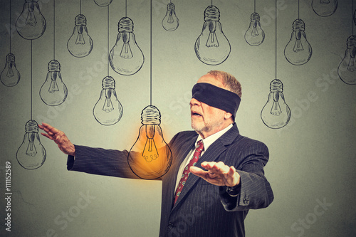 Fotografie Blindfolded senior man walking through light bulbs searching for bright idea