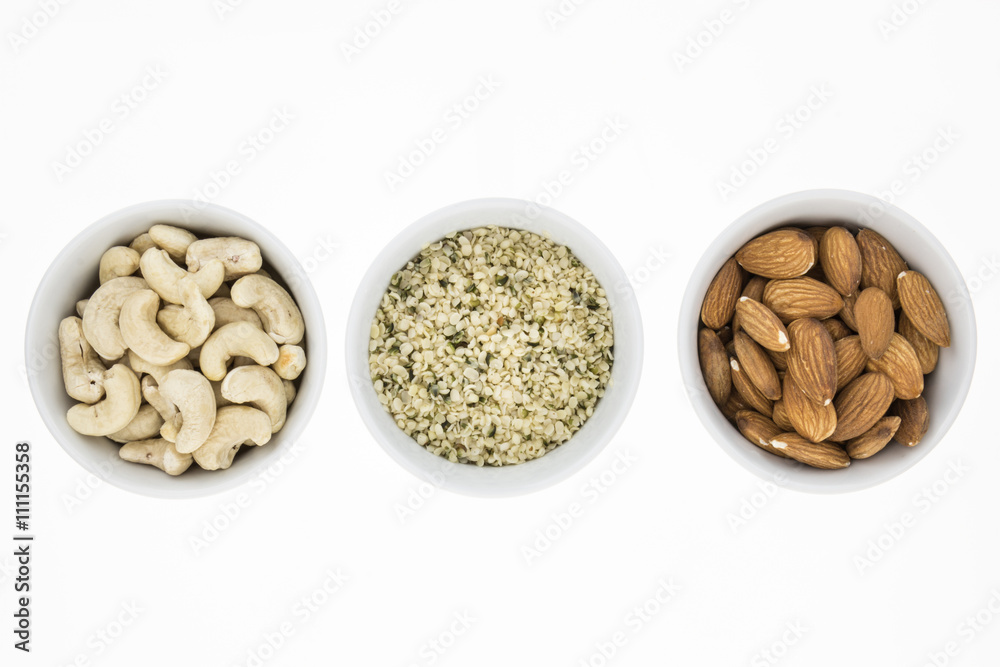 Cashews, hemp meal and unblanched almonds in bowls, on white background Cashews, hemp meal and unblanched almonds in bowls, on white background