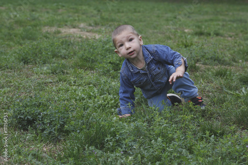 Small child is risign with one hand from the grass