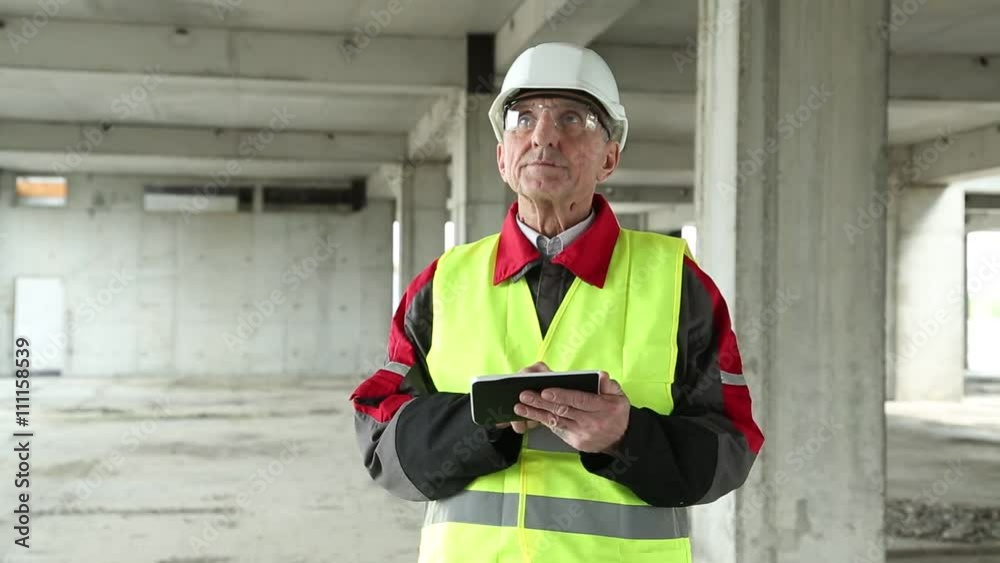 Master builder in white hard hat with Tablet PC at construction site. Manager of the works with electronic device at construction site. Building supervision. Worker in white helmet at project site Master builder in white hard hat with Tablet PC at construction site. Manager of the works with electronic device at construction site. Building supervision. Worker in white helmet at project site