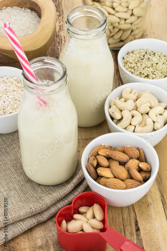 Bottles of homemade plant based milk and bowls with ingredients, on wooden background