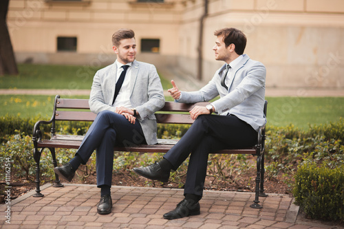 Two stylish businessmen speaking and smiling outdoors