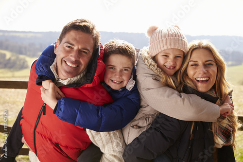 Parents piggy back kids in the countryside looking to camera