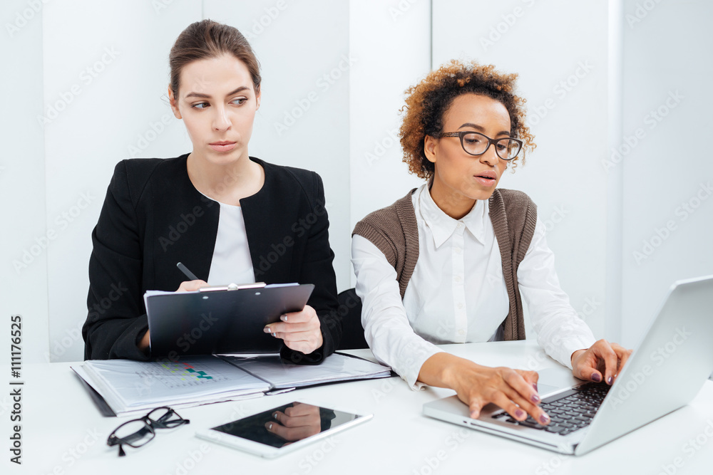 Two focused businesswomen working using clipboard and laptop Two focused businesswomen working using clipboard and laptop