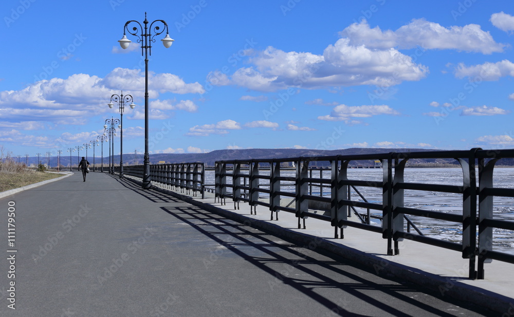 empty pier and calm water on a background of blue sky and clouds. beautiful fence and pillars. Woman goes forward
