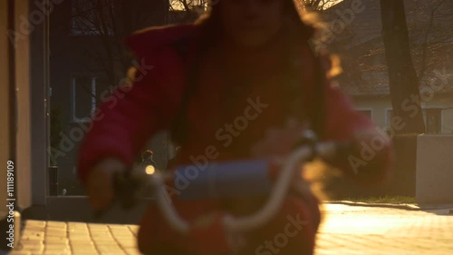 Little Girl is Riding a Bicycle by City Street People Silhouettes in the Evening Sunset Girl's Silhouette in the Sun Paving Stones Kid is Learning to Ride