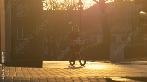 Little Girl Starts to Ride a Bicycle by City Street in the Evening Sunset Girl's Silhouettes in the Sun Paving Stones Kid is Learning to Ride a Bike