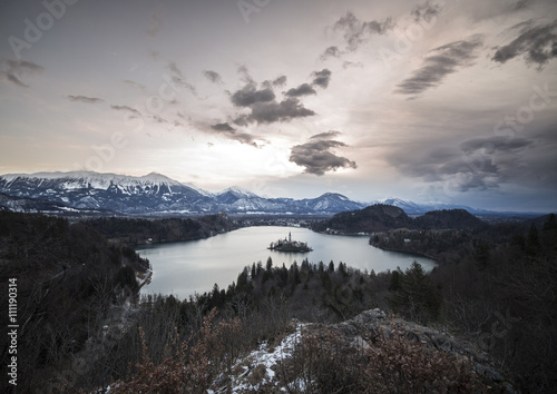 Panoramic view of island with church in the middle of Lake Bled among the mountains in snow.