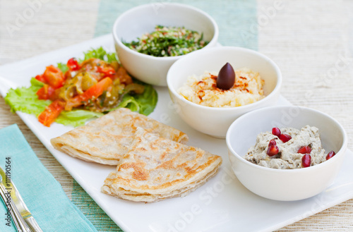 Assortment of dips: hummus, chickpea dip, tabbouleh salad, baba ganoush and flat bread, pita on a plate