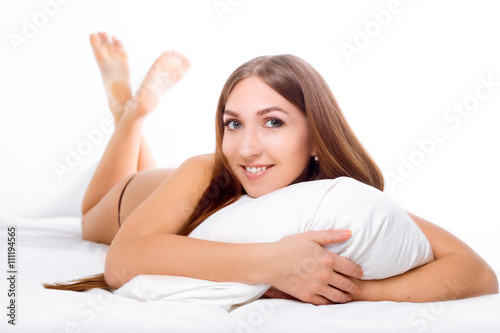 The woman lies on the edge of the bed and smiling , with her head resting on the pillow . The hands are under the pillow. 