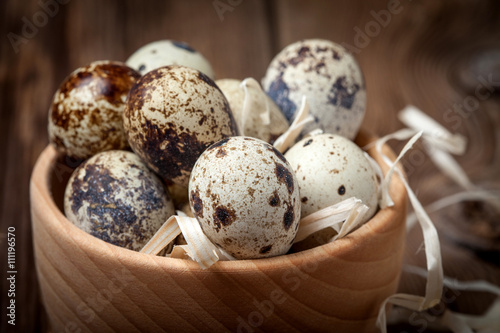 Raw quail eggs in a wooden bowl on wooden table.