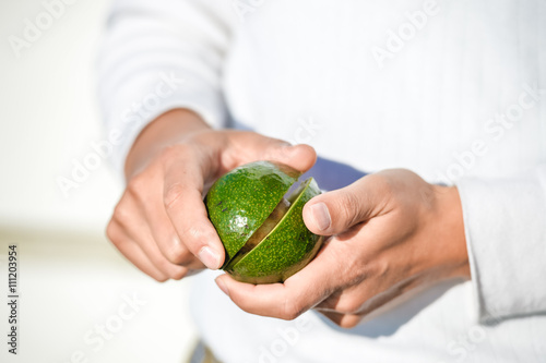 Hands holding fresh avocado cut in half on light background. Closeup 