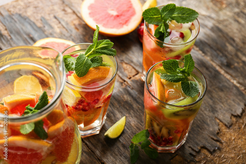 Refreshing cocktails with ice, mint, pomegranate seeds and slices of fruits on rustic wooden background