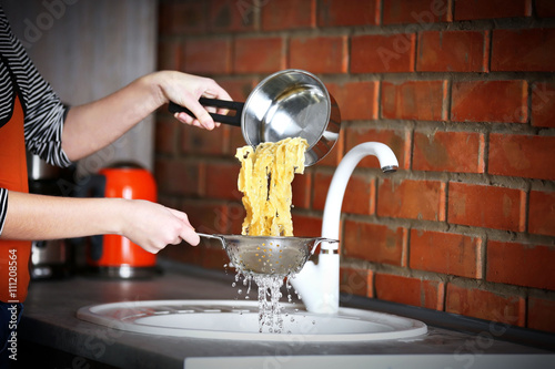 Female hands pouring water from boiled pasta over sink in the kitchen