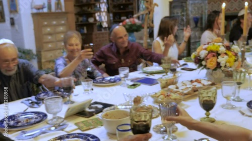 A man wearing a yarmulke leads a toast at a large dinner table