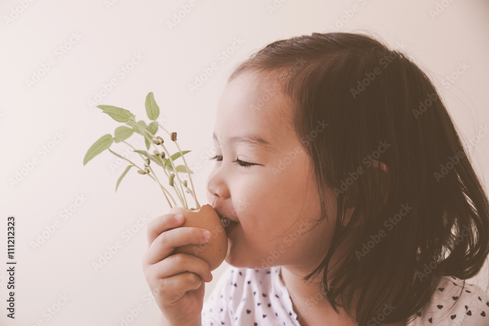 A toddler girl holding and kissing young plants in eggshell, eco A toddler girl holding and kissing young plants in eggshell, eco