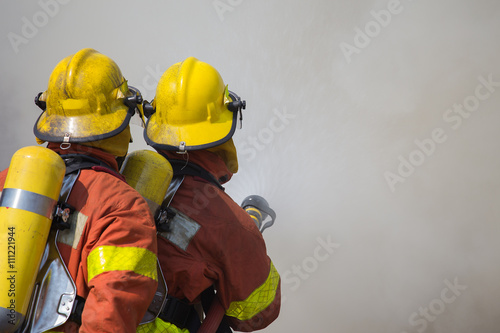 2 firemen spraying water in fire and smoke