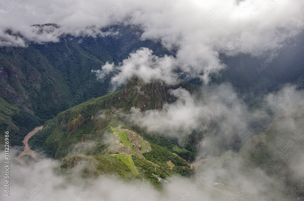 View of the Lost Incan City of Machu Picchu and Huayna Picchu mountain from Machu Picchu mountain .Low clouds .Cusco Region,Sacred Valley, Peru