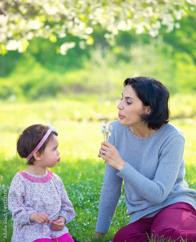 Mother with small daughter blowing to dandelion - lifestyle outdoors scene in park Mother with small daughter blowing to dandelion - lifestyle outdoors scene in park