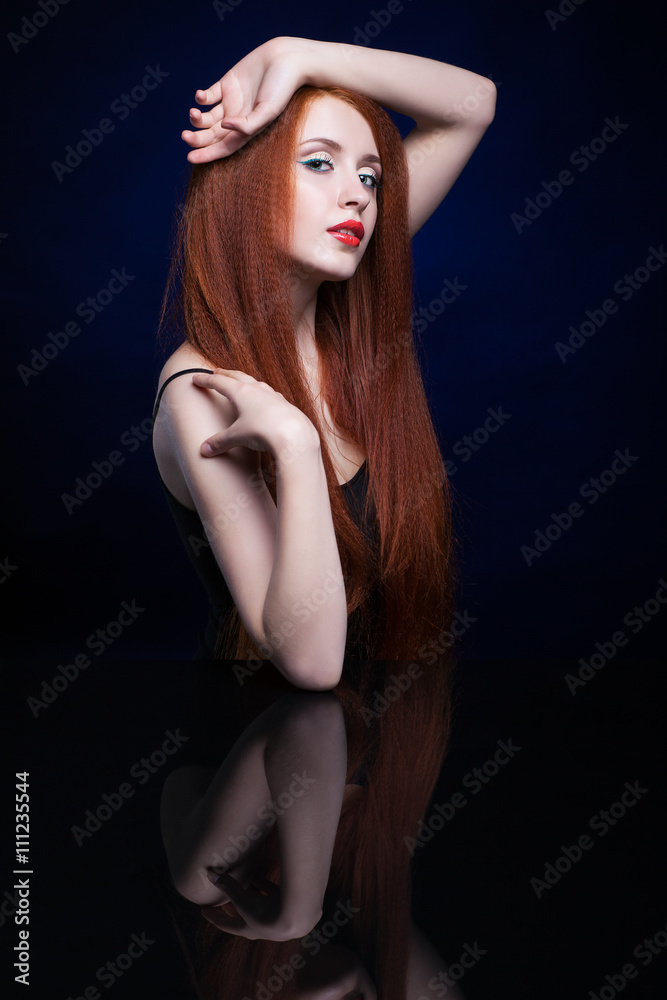 Young woman with ginger hair over reflection mirror on blue back Young woman with ginger hair over reflection mirror on blue back