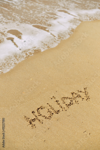 Top view on inscription Holiday on sea sand beach with the sun rays against wave foam. vacation concept