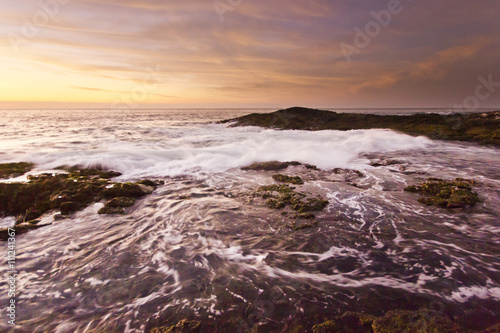 golden sunset at pacific ocean with waves on rocky shore