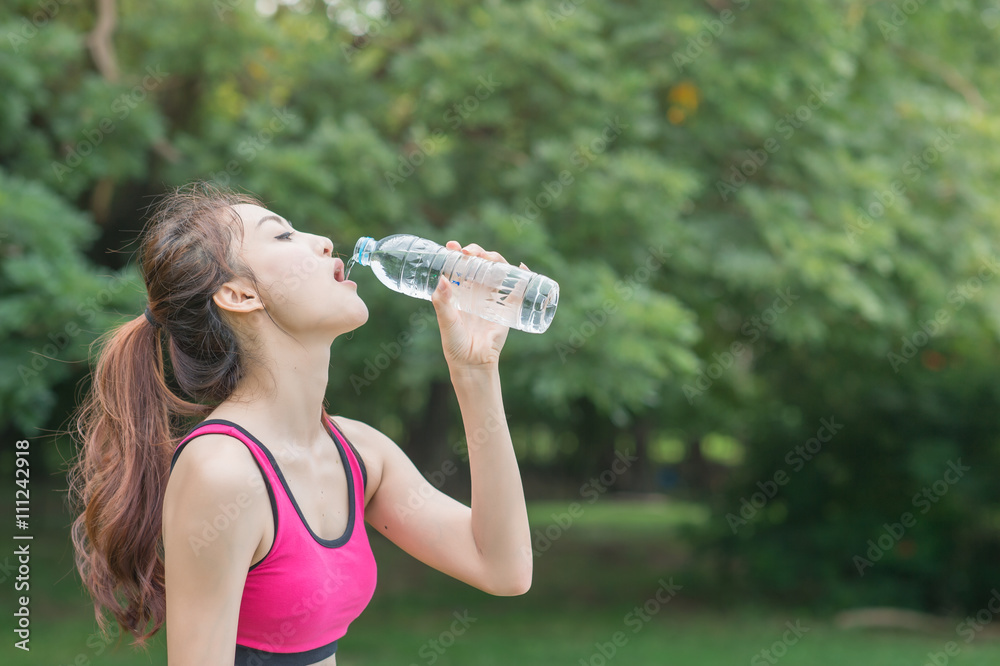 young attractive woman drinking water from plastic bottle in the park young attractive woman drinking water from plastic bottle in the park