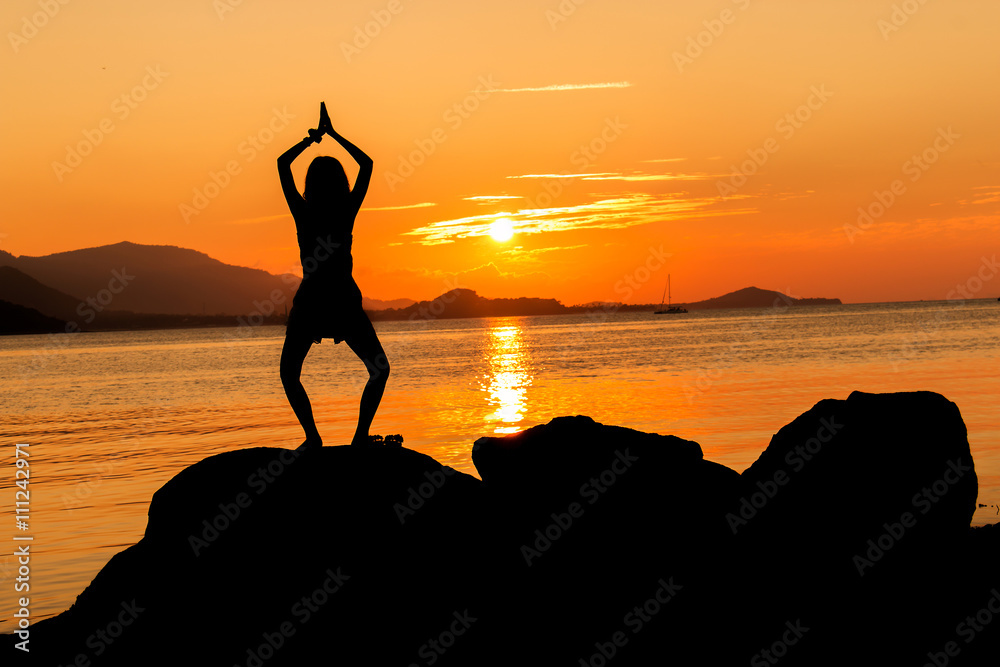 Silhouette of young woman practicing yoga on the beach sunset ba